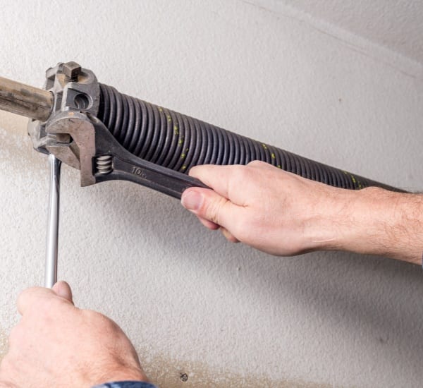 Hands adjusting garage door spring mechanism at home workshop during daylight hours