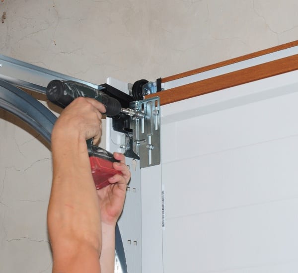 Installation of a garage door with a power drill by a worker at a residential location during daylight hours