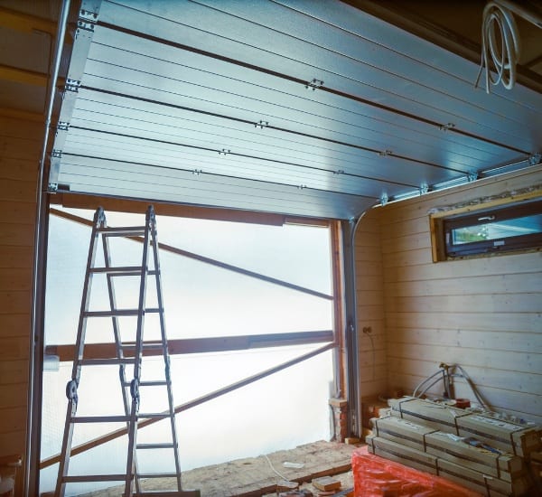 Construction of a modern garage door with aluminum panels and ladder inside a workshop