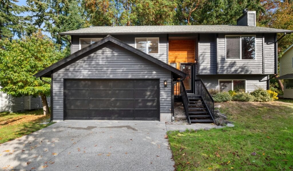 Modern gray house with wooden accents surrounded by lush trees in a suburban neighborhood during autumn