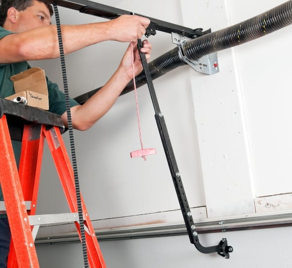 Technician repairing a garage door mechanism while standing on a ladder in a residential garage