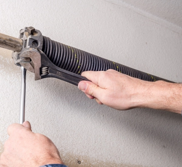 Hands adjusting garage door spring mechanism at home workshop during daylight hours