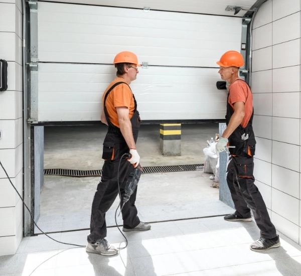 Two workers repair a garage door in a construction site during daylight hours