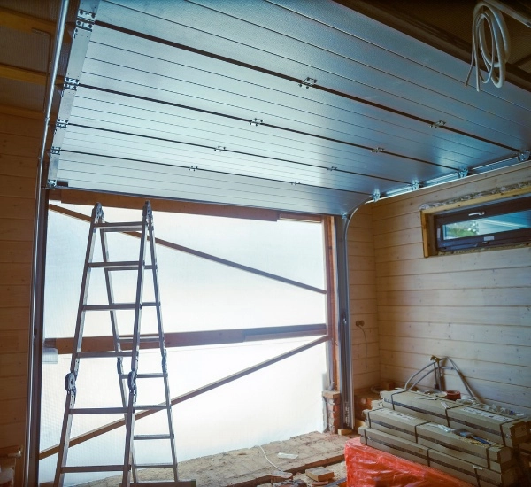Construction of a modern garage door with aluminum panels and ladder inside a workshop