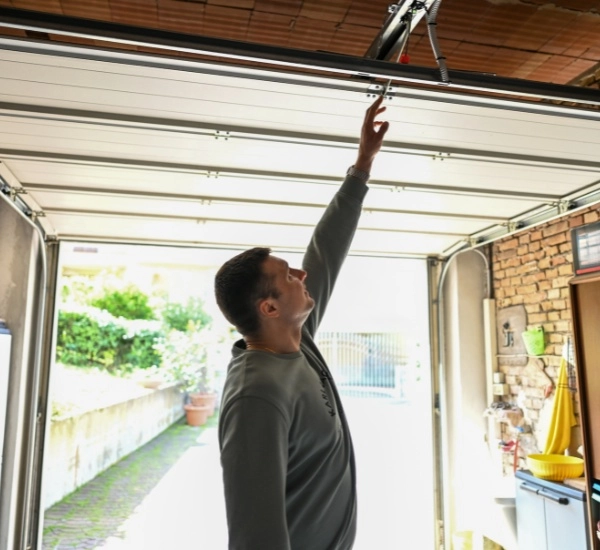 Man reaching up to adjust garage door mechanism in residential garage during daylight hours